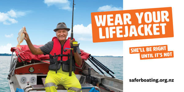Man wearing lifejacket on boat with a fish he has caught. 