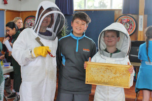 Photograph of 3 students. Two of them wearing beekeeping masks and clothing. 