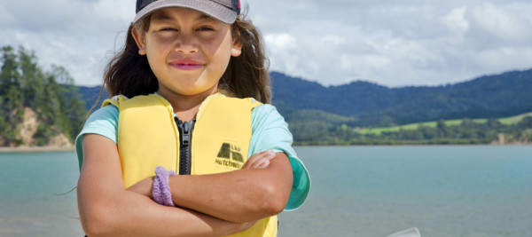 A child stands by the water wearing a lifejacket